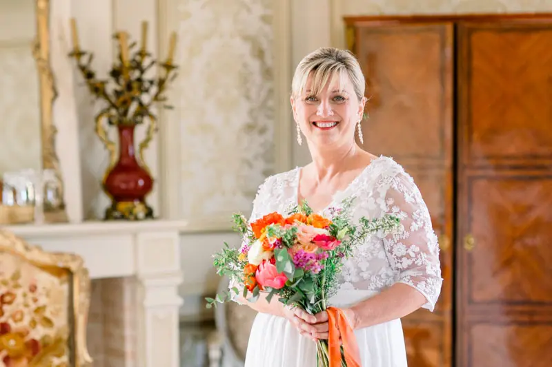 Bride holding her bouquet with orange ribbons beside a fireplace