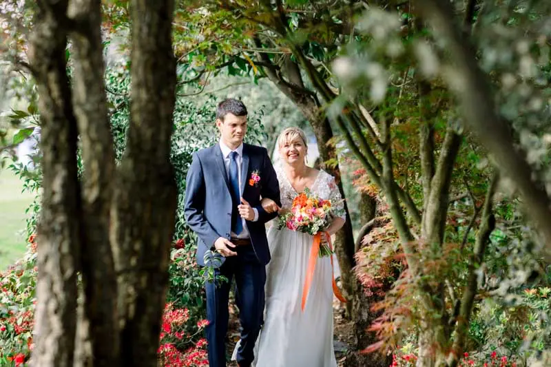 Bride walking in on a loved one's arm through the wooded grounds