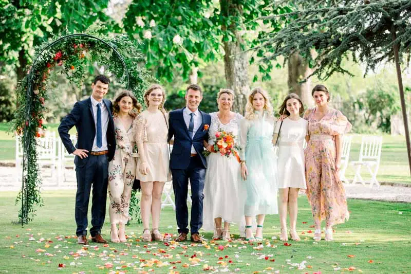 Bride and groom posing with loved ones beneath the floral ceremony arch