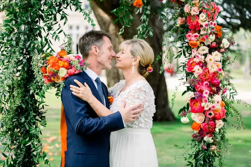 Bride and groom kissing, framed by the floral arch at Château Pape Clément