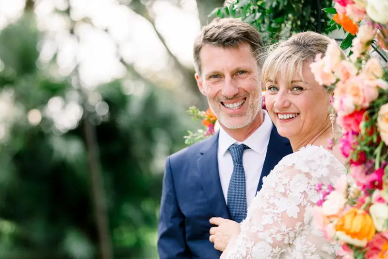 Smiling bride and groom beneath the floral arch at Château Pape Clément