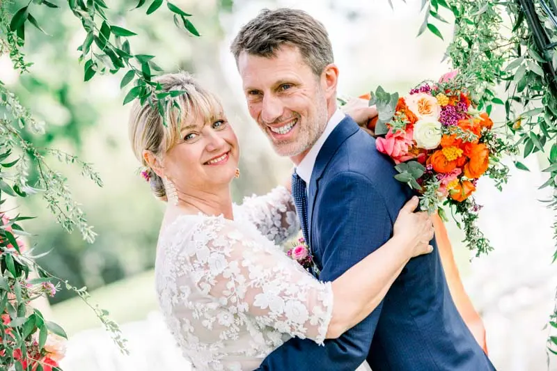Bride hugging the groom as he holds her vibrant bouquet