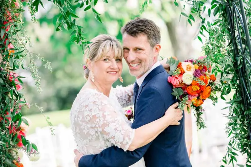 Hélène and Christophe cheek to cheek beside the flower arch