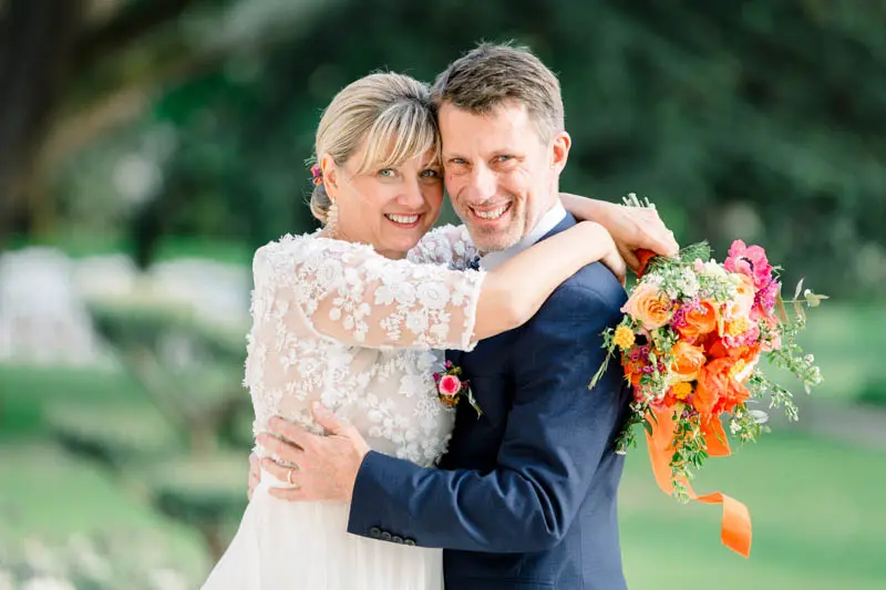 Bride and groom hugging and laughing, orange bouquet in hand