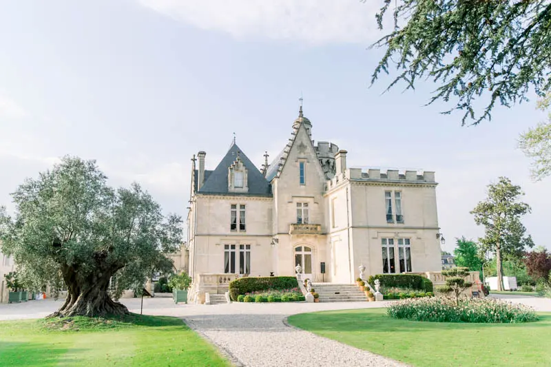 Gothic Revival facade of Château Pape Clément and its olive tree under blue sky