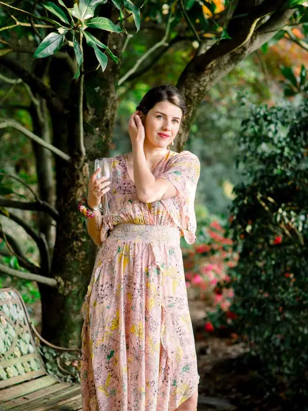 Guest in a long pink dress posing before a flowering shrub