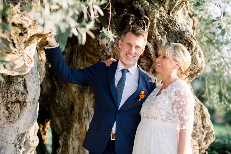 Bride and groom laughing beneath an ancient olive tree in the grounds