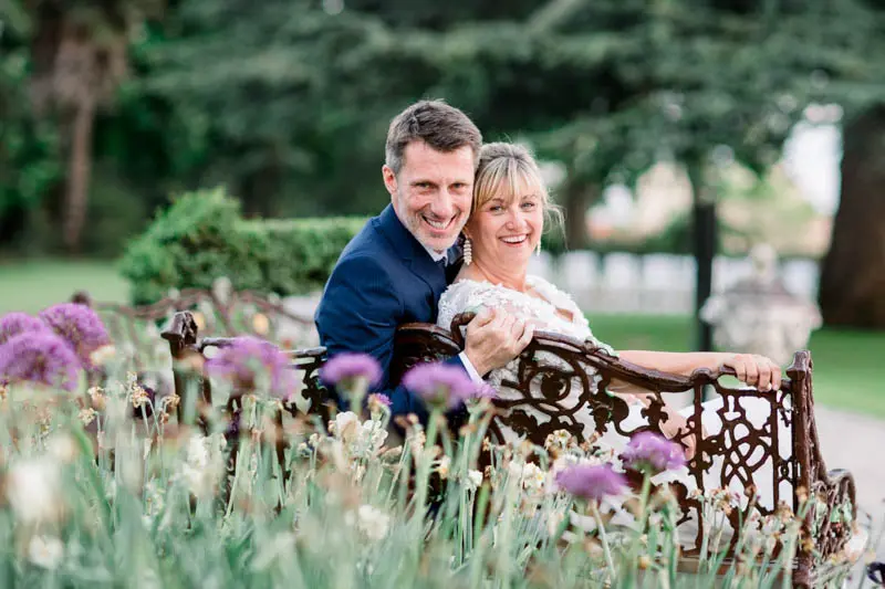 Bride and groom sitting on a wrought-iron bench behind allium flowers