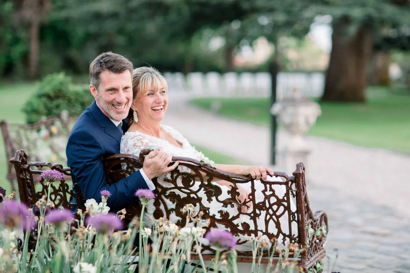 Bride and groom laughing on a wrought-iron bench in the grounds of Château Pape Clément