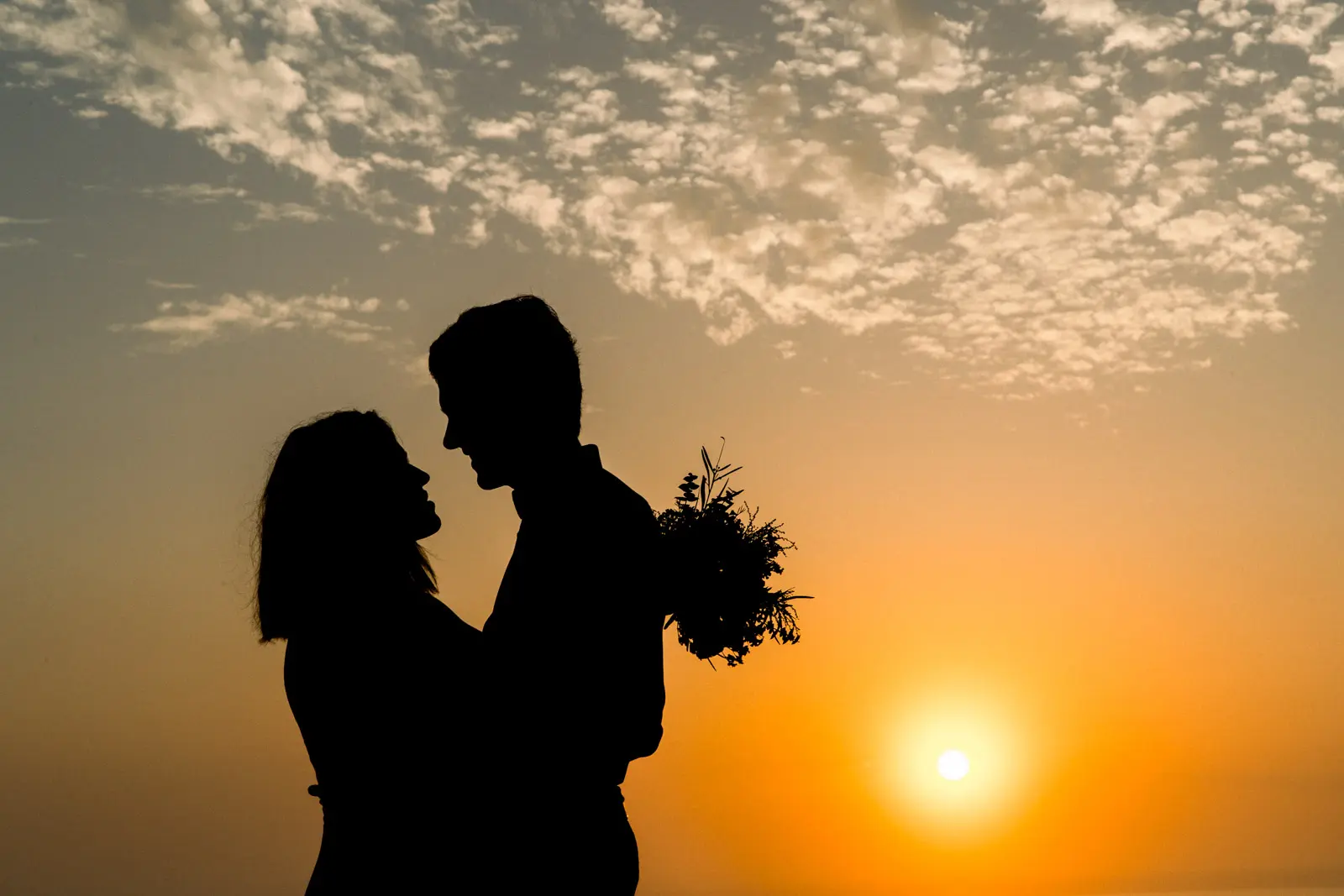 Silhouette of a couple embracing against an orange sunset