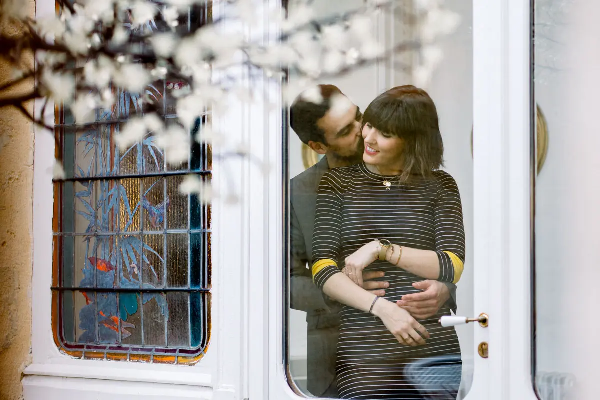 A man hugging his partner from behind in front of a stained glass door