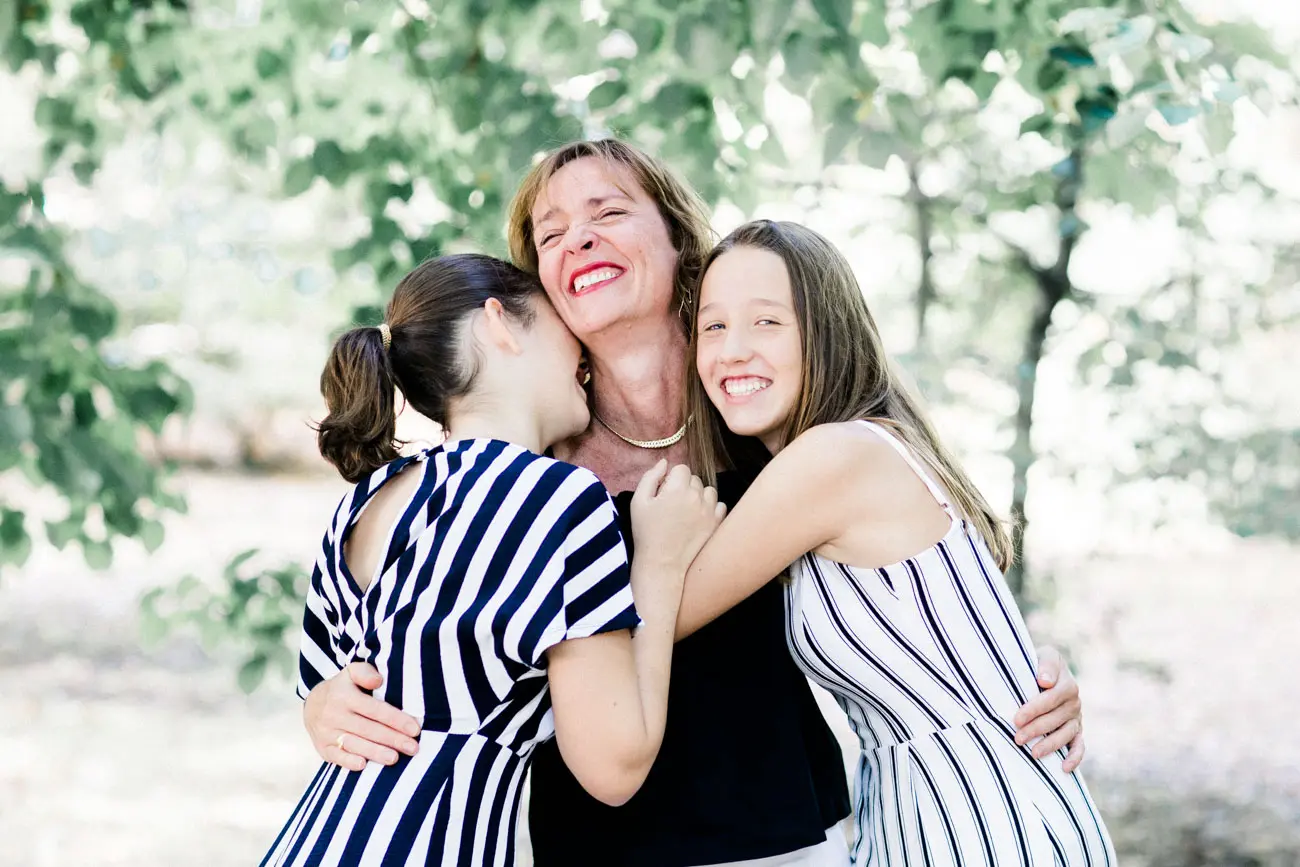 Mother hugged by her two laughing daughters at the Parc Bordelais