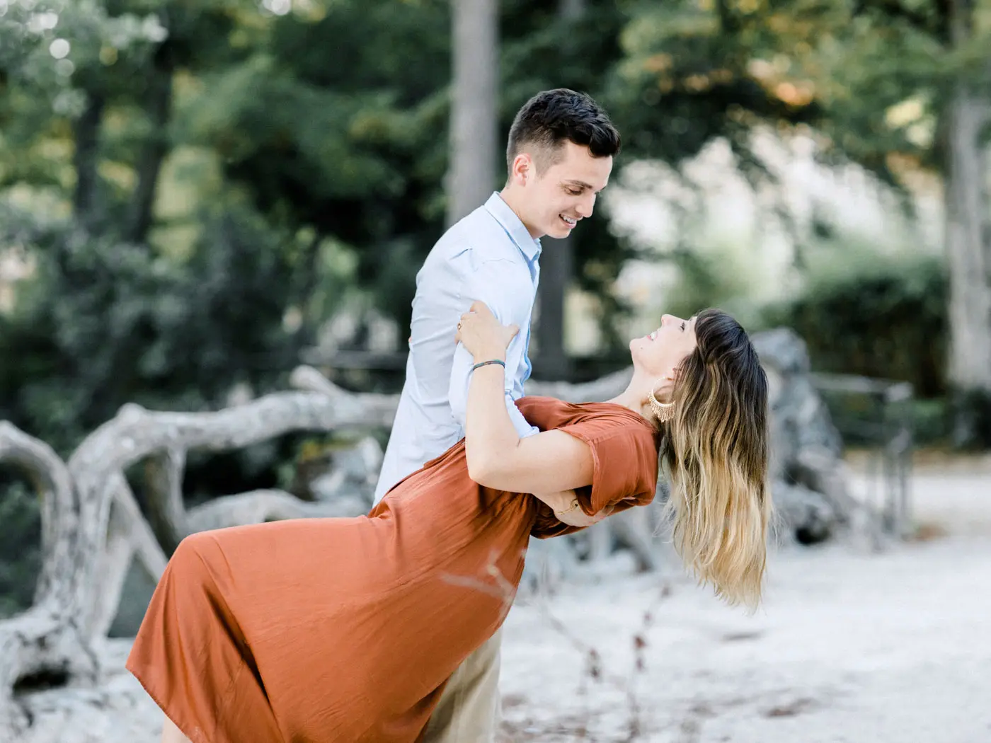 Man dipping his partner in a rust-coloured dress in a shady park