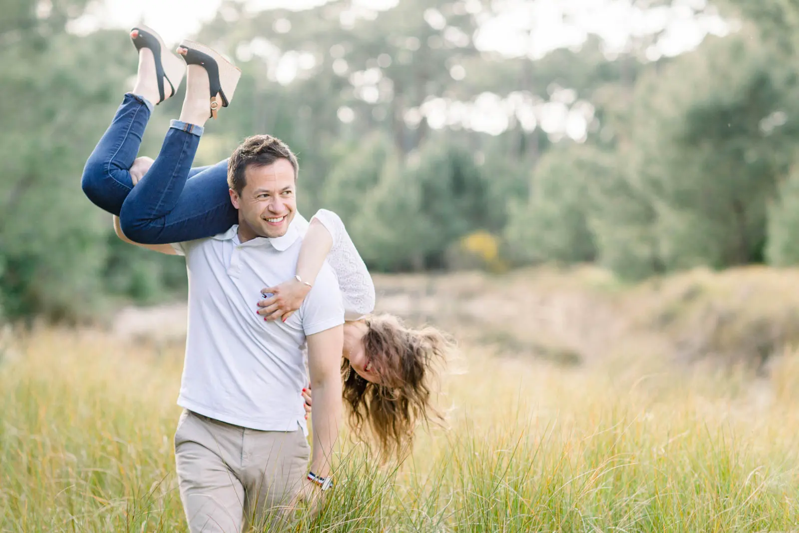Man carrying his partner upside down over his shoulder in tall grass