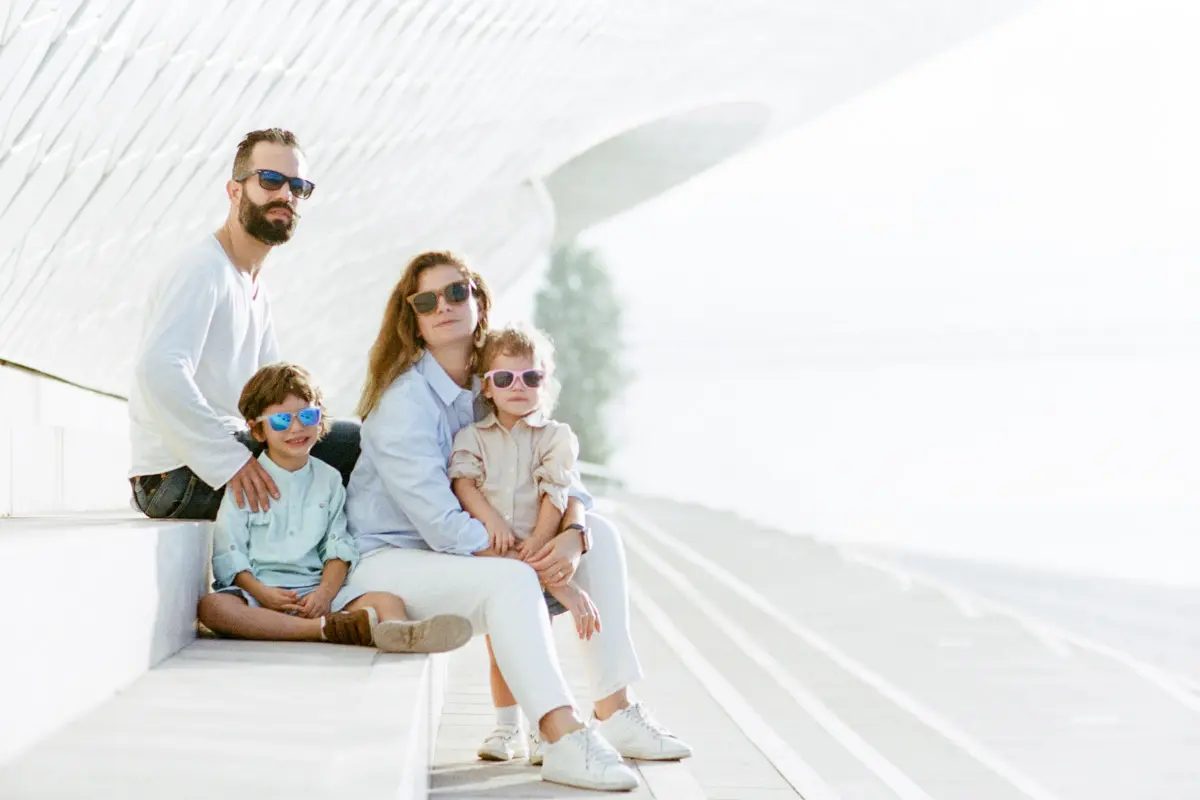 A family with two children in sunglasses sitting on white steps in Lisbon