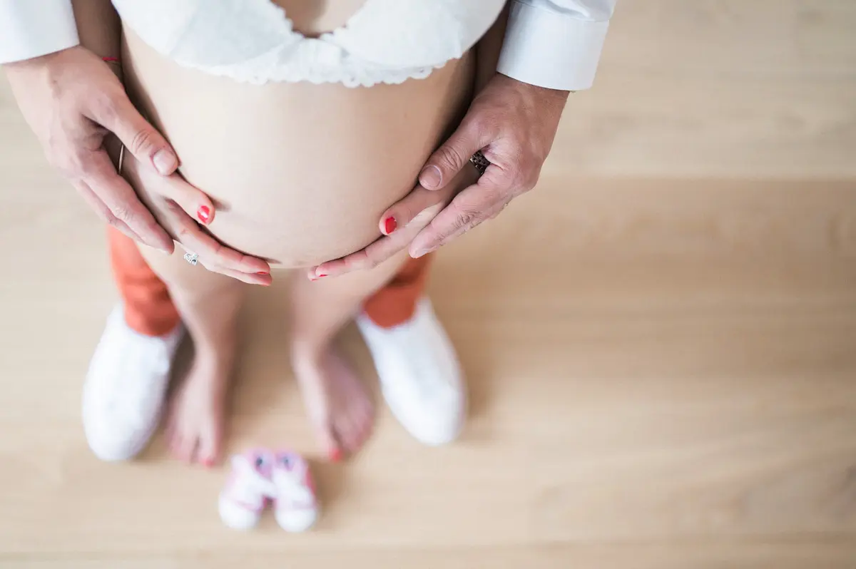 Mains des futurs parents sur le ventre rond, petits chaussons au sol
