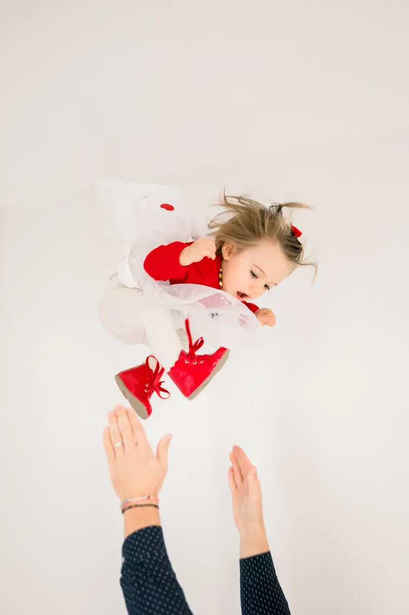 Little girl in red tossed in the air by her dad's hands