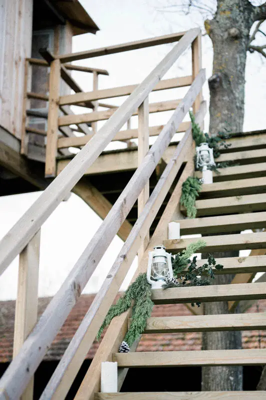 Wooden treehouse staircase decorated with lanterns and fir branches