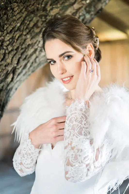 Bride in a lace gown and white fur stole, hand raised to her face