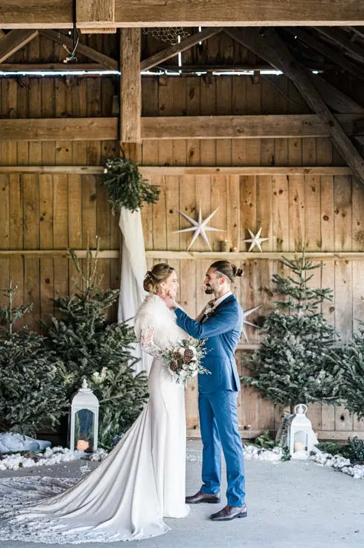 Bride and groom embracing in the wooden barn decorated with firs and stars