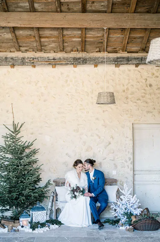 Bride and groom sitting on a bench beside a fir tree in a stone room