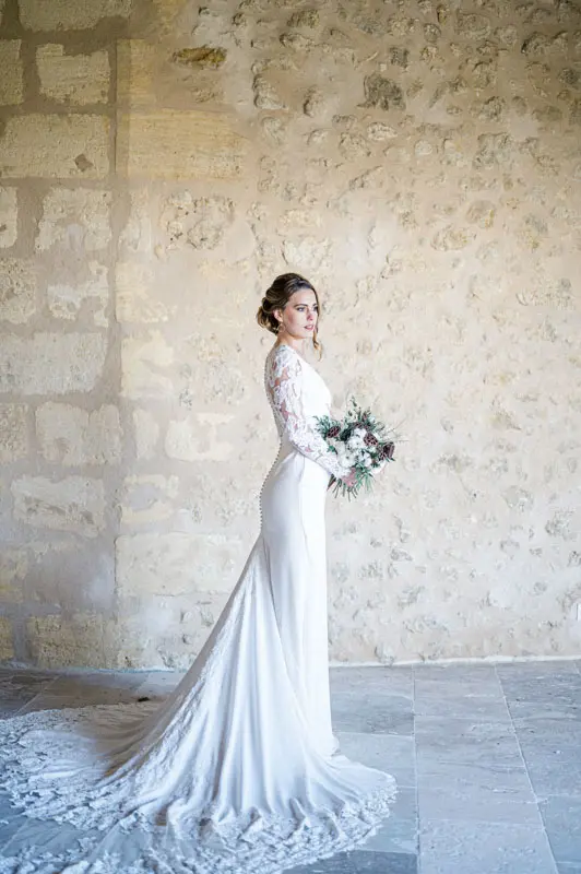 Bride in a gown with a long train against a pale stone wall