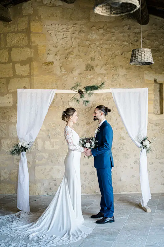 Bride and groom facing each other under an arch of white drapes and fir