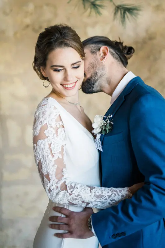 Smiling bride nestled against the groom in front of the stone wall