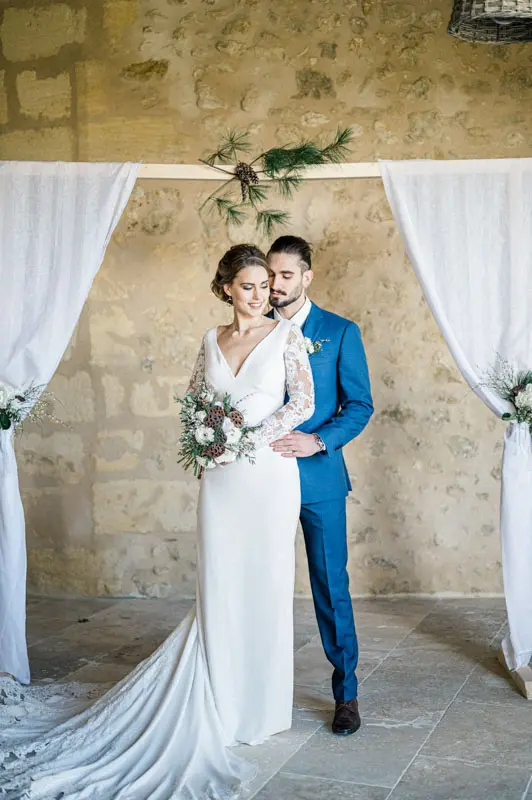 Bride and groom posing beneath the draped arch against the stone wall