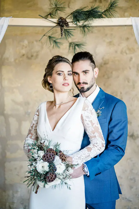 Groom hugging the bride from behind, bouquet of white flowers and pine cones