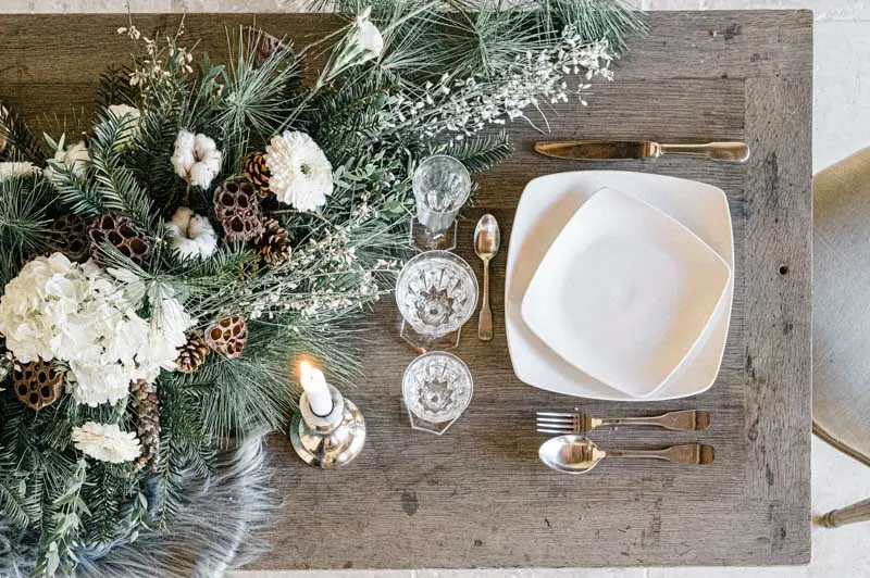 Overhead view of a winter table setting with a white plate, glasses and flowers