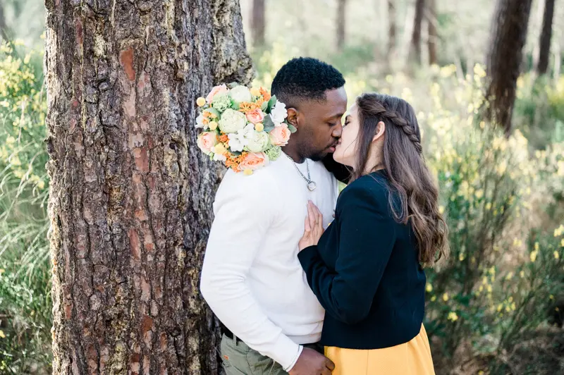 The couple kissing against the trunk of a tall maritime pine