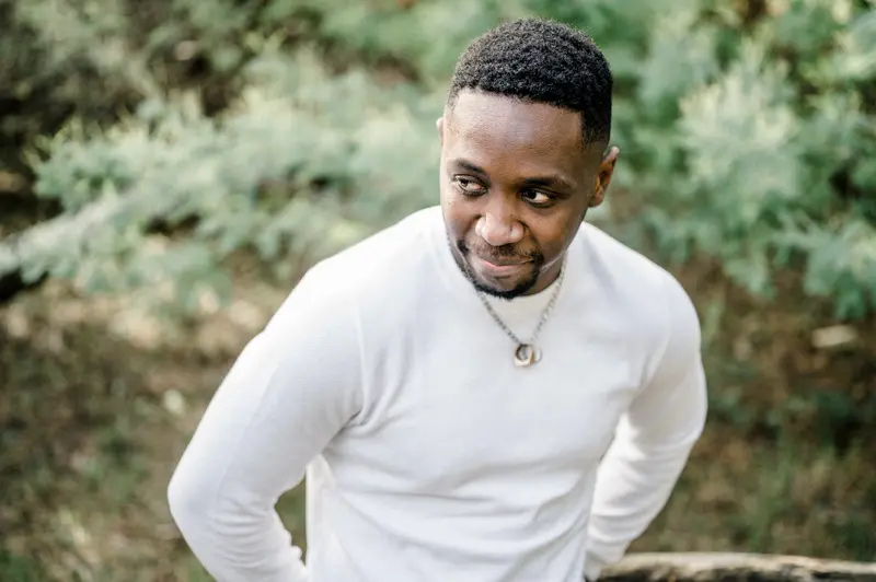 Portrait of the groom-to-be in a white sweater, looking down among the pines