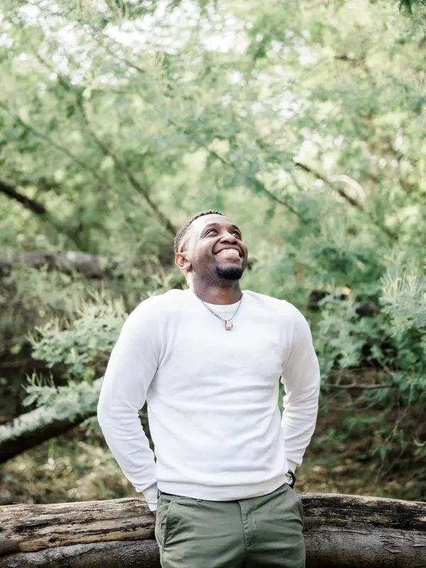 The groom-to-be in a white sweater smiling on a log in the forest