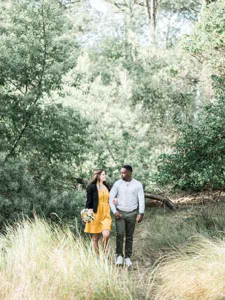 The couple hand in hand among tall grasses in the forest