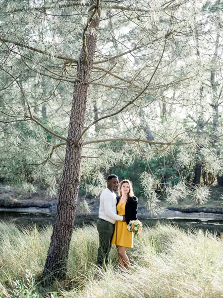 The couple standing by a pine at the edge of a forest pond