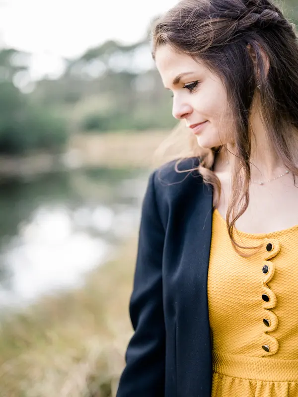 The bride-to-be in a mustard yellow dress, in profile by the water