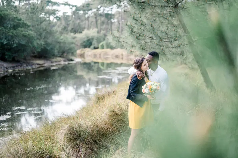 The couple embracing by the pond, seen through the foliage
