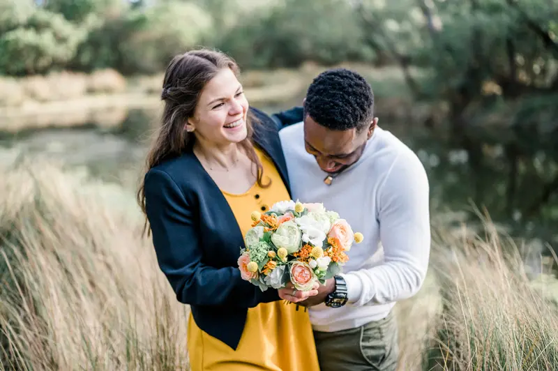 The couple laughing in a close embrace among the waterside grasses