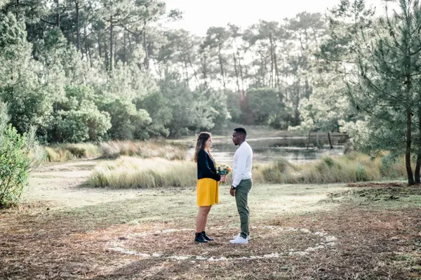 The couple facing each other in a clearing surrounded by pines
