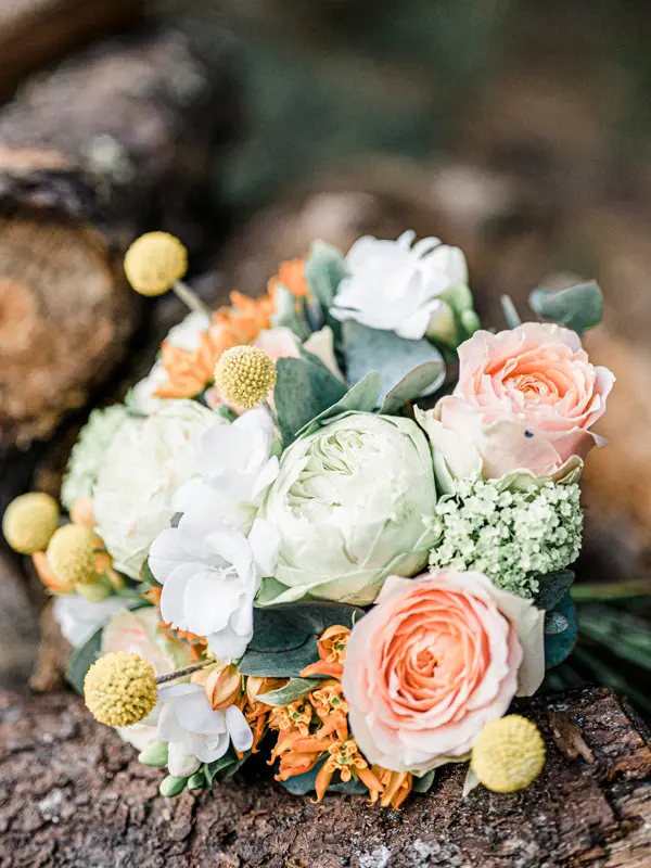 Bouquet of peach roses, yellow billy buttons and white blooms resting on wood