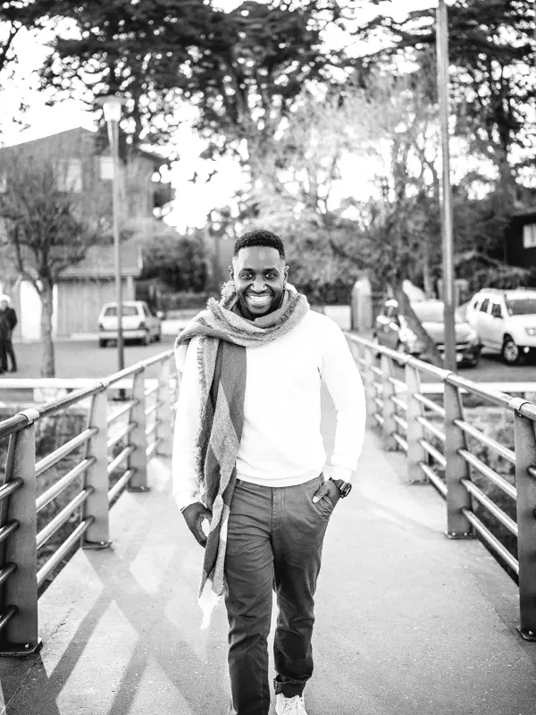 The smiling groom-to-be in a scarf on the jetty, in black and white