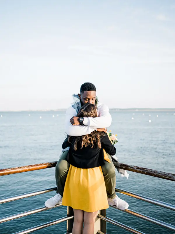 The bride-to-be in her partner's arms as he sits on the railing