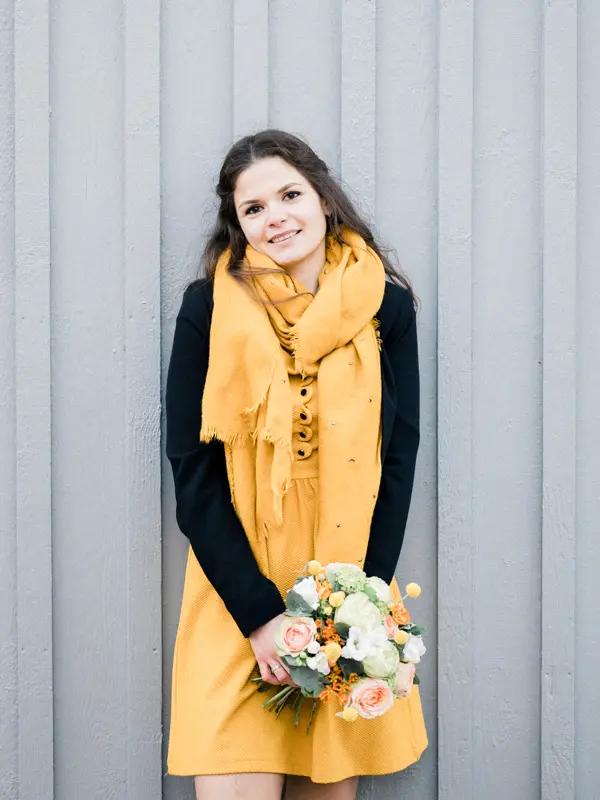 The bride-to-be in a yellow dress leaning against a grey hut