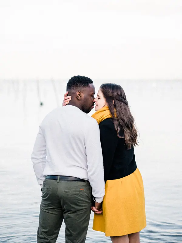 The couple embracing at the water's edge with oyster stakes behind
