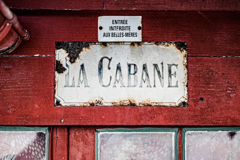 "La Cabane" plaque and a humorous sign on a red wooden door