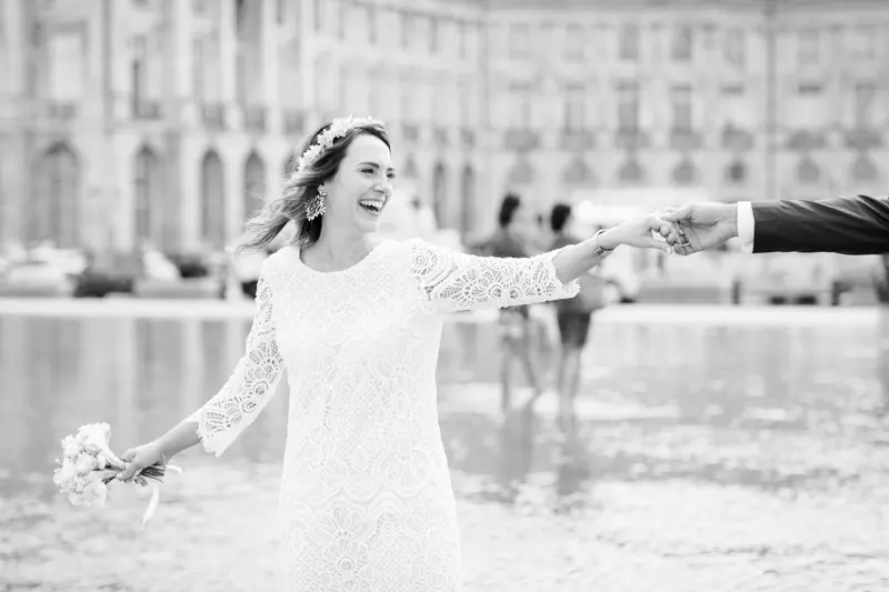 The bride leading the groom by the hand across the Bordeaux water mirror