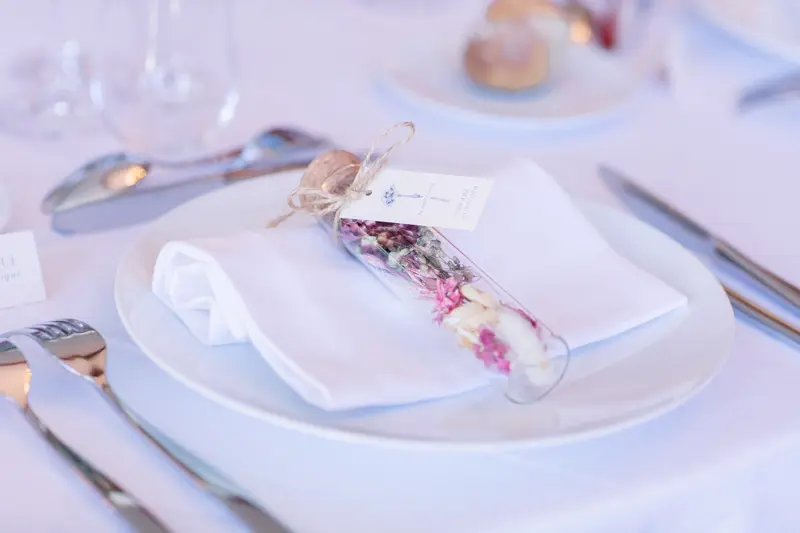 Place setting with a guest favour of dried petals in a glass tube