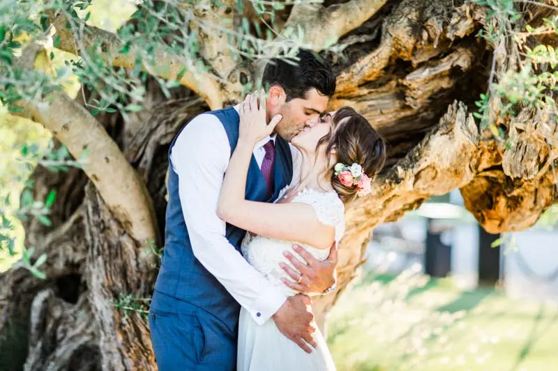 Caroline and Giovanni kissing against an old olive tree at Château Pape Clément
