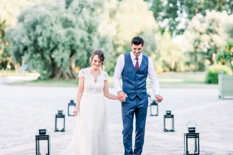 The bride and groom walking between black lanterns in the château grounds